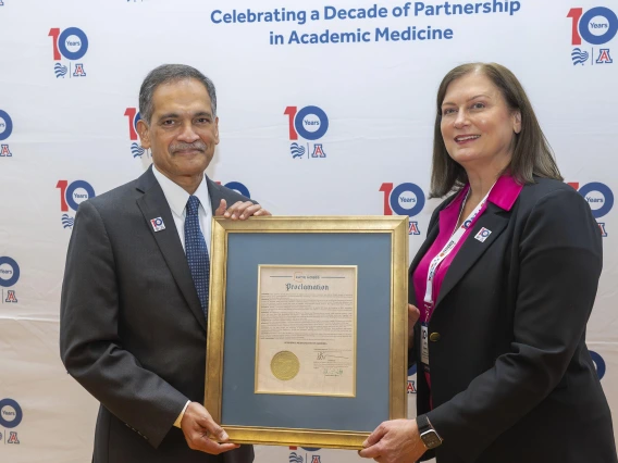 Suresh Garimella and Amy Perry each holding one side of a framed proclamation in front of a white backdrop with red and blue logos for U of A and Banner Health
