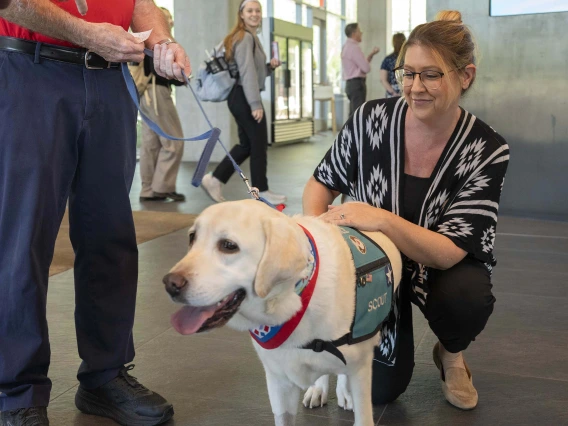 Amy Barber squats next to Scout, a yellow Lab, with one hand on the dog’s back.