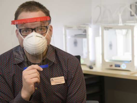 Tory Middlebrooks, of University Libraries, models a face shield, which is designed to be worn in conjunction with additional PPE such as a mask. Middlebrooks mans the 3D printers that produced the headbands for the face shield.