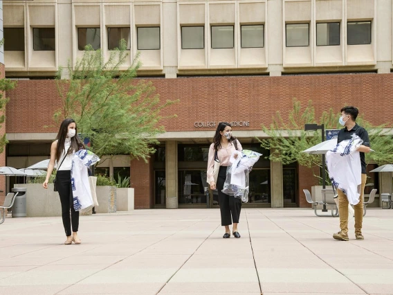 White coats in hand, three new members of the Class of 2024 leave the College of Medicine – Tucson building. From left: Lupita Molina, Julia Alvarenga Couto and Lawrence Sun.