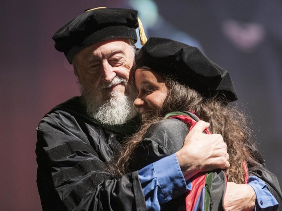 Retired professor Craig McClure, MD, hugs Faith Dickerson, MD, after hooding her during the College of Medicine – Tucson class of 2022 convocation at Centennial Hall. 