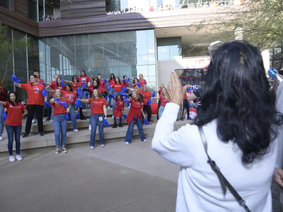 Back of a woman witih dark brown hair taking a photo of dancers performing on a small stage.