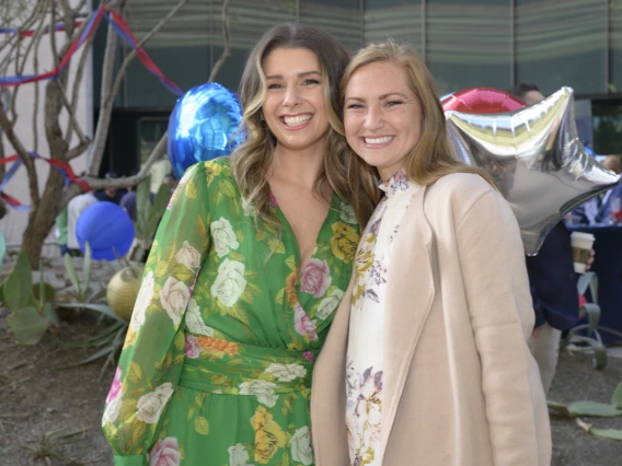 Two young adult women hug sideways and smile. 