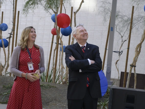 A middle-aged woman with blonde hair stands next to an older man with gray hair. Both are looking up to the right and smiling. 