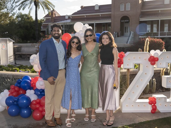 Four people with brown skin stand in front of a large 2023 sign smiling with their arms around each other.