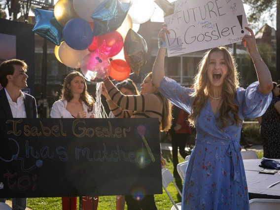 Young woman in blue dress smiling big holds a sign that reads "Future Dr. Gossler"