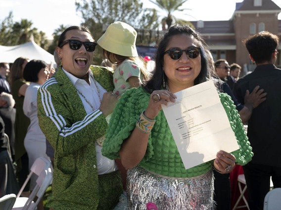 A woman in sun glasses holds a letter while smiling and her husband and child are in the background. 