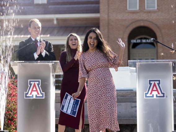 Young woman with long dark hear in a dress cheers in front of two podiums with Arizona As on them.