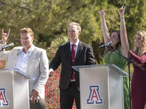 A young adult man and woman each stand at an Arizona podium with arms and hands raised in celebration. 