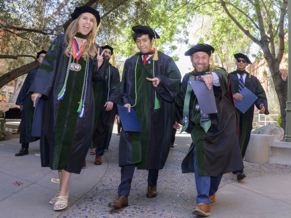 Several pharmacy students in graduation regalia smile as they walk outside after their graduation ceremony.