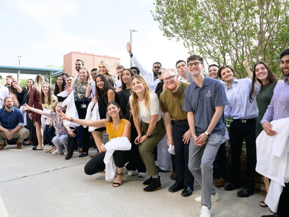 A large group of medical students stand in a line outside smiling and waving. 