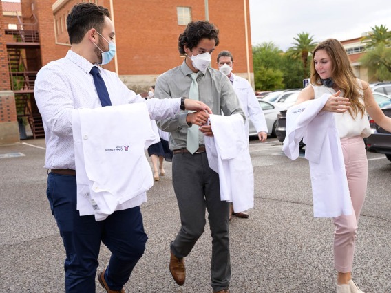 Members of the UArizona College of Medicine – Tucson Class of 2026 discuss how to properly fold their coats as they walk to the ceremony at Centennial Hall.