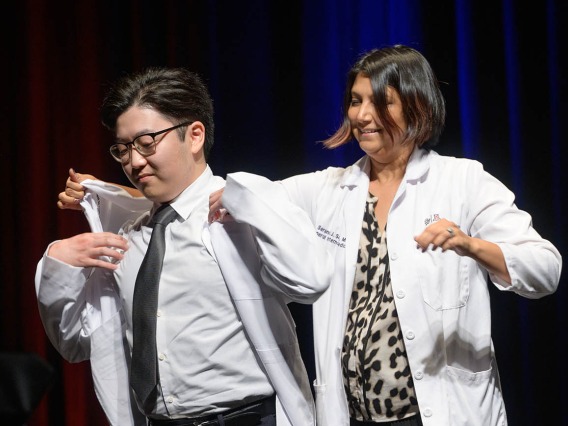 Andrew Endo is given his white coat by Serena Scott, MD, assistant professor of medicine, at the UArizona College of Medicine – Tucson Class of 2026 white coat ceremony.