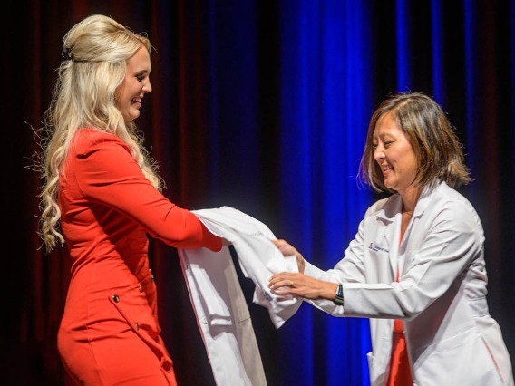Hailey Patterson prepares to be coated by Alice Min, MD, FACEP, associate dean for career development, at the UArizona College of Medicine – Tucson Class of 2026 white coat ceremony. 