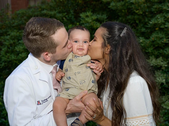 Spencer Holmes and his wife, Aiysha Holmes, celebrate his new white coat by kissing their baby, Eli, after the UArizona College of Medicine – Tucson Class of 2026 white coat ceremony.