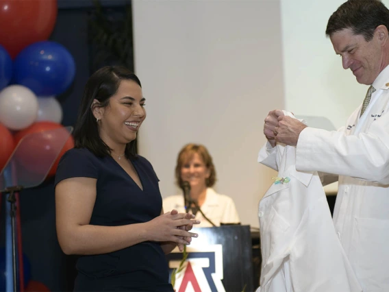 Brenda Valencia Gonzales is presented her white coat by Kevin Moynahan, MD, FACP, vice dean of education at the UArizona College of Medicine – Tucson. 