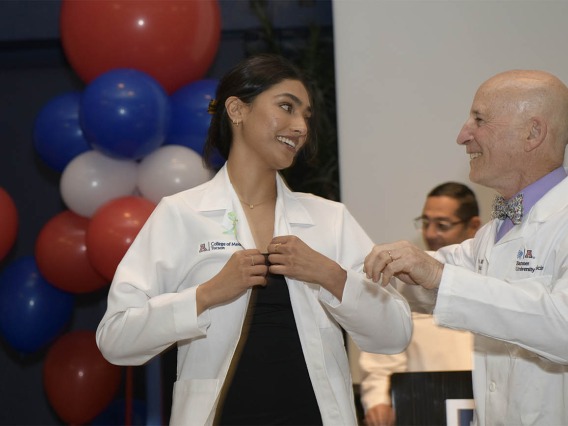 Meghana Partha puts her white coat on after it was presented to her by Paul Gordon, MD, MPH, co-director, Bachelor of Science in Medicine, at the UArizona College of Medicine – Tucson.