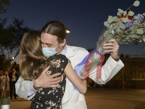 Benjamin Nichols receives flowers and a hug from his partner after his UArizona College of Medicine – Tucson class of 2024 white coat ceremony.