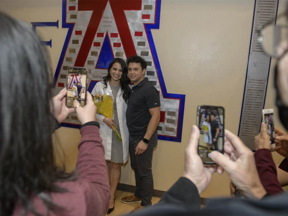 Lupita Molina poses in her new white coat with Blaze Rose as family members take photos after the UArizona College of Medicine – Tucson’s class of 2024 white coat ceremony.