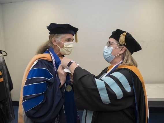 Lisa Kiser, DNP, MSN, (left) is helped with her hood by Erin McMahon, EdD, CNM, FACNM, before the start of the UArizona College of Nursing 2022 spring convocation at Centennial Hall. 