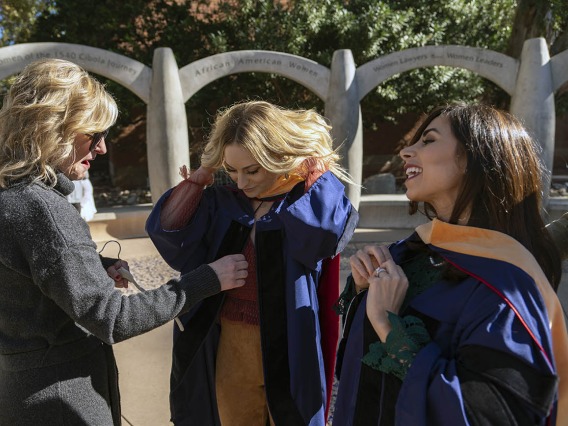 Kristine Harmon (left) helps her daughter, Erika Harmon with her graduation gown as Sheema Zarezadeh buttons up her gown (right) before the College of Nursing fall convocation at Centenial Hall.