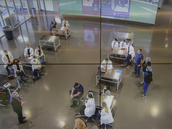 University of Arizona President Robert C. Robbins, MD, (lower left) as seen through four monitors in the Arizona Simulation Technology and Education Center control room, speaks with the second-year CRNA students and faculty between simulations for their clinical skills intensive.  