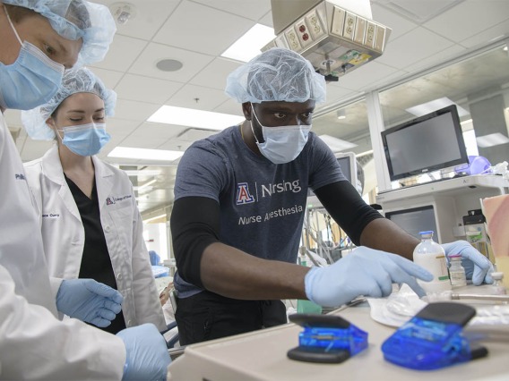 CRNA students Olu Bello, RN, (right) grabs medication to administer to the “patient” while Anastasia Connelly, RN, and Phillip Bullington, RN, keep an eye on the monitor during a critical skills simulation in the Arizona Simulation Technology and Education Center.