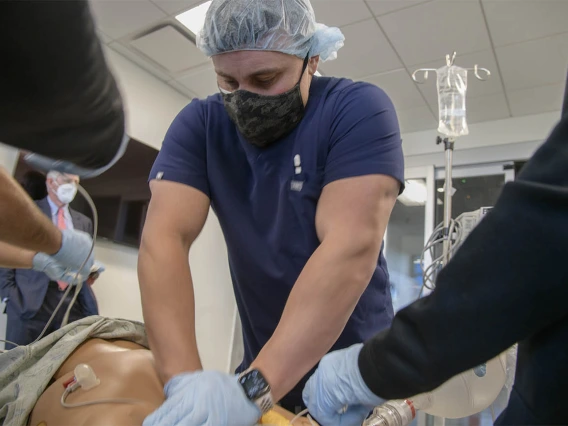 John Mougin, RN, performs chest compressions on a manikin during a CRNA critical skills intensive simulation in the Arizona Simulation Technology and Education Center, while University of Arizona President Robert C. Robbins, MD, observes in the background. 