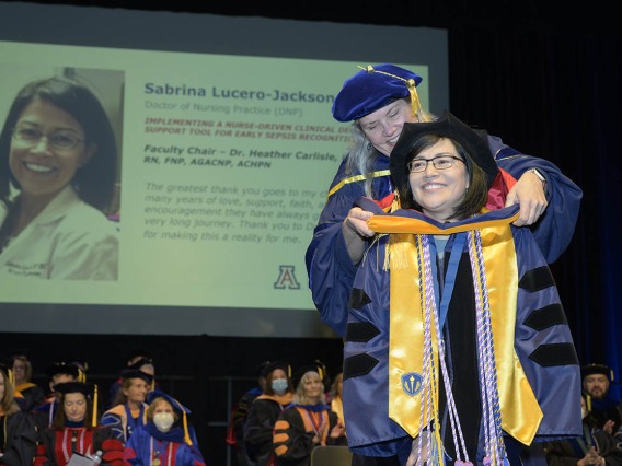 Sabrina Lucero-Jackson is hooded by associate professor Heather L. Carlisle, PhD, DNP, RN, FNP, AGACNP, CHPN, during the UArizona College of Nursing fall convocation for earning a Doctor of Nursing Practice degree.