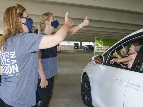 Staff from the All of Us Research Program give a thumbs up to a carload of visitors to demonstrate how “hitchhiker’s thumb” is an example of an inherited genetic trait.