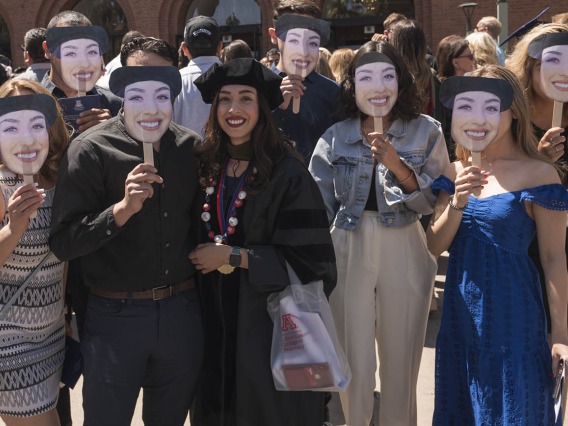 Daisy Arellano, PharmD, poses for a photo with her family – who all hold up photos of her face – after the R. Ken Coit College of Pharmacy 2022 spring convocation at Centennial Hall.  
