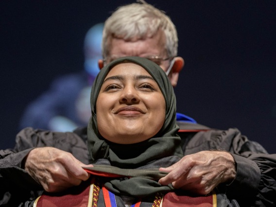 Ahlam Althobaiti, PharmD, is hooded by John Regan, PhD, for earning her Doctor of Pharmacy degree during the R. Ken Coit College of Pharmacy 2022 spring convocation at Centennial Hall.