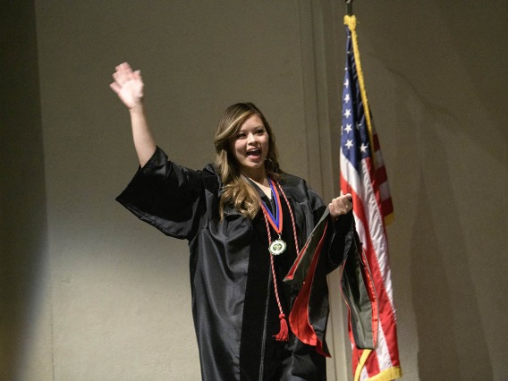 Diana Pham, PharmD, waves to the audience as she walks across the stage to be hooded during the R. Ken Coit College of Pharmacy 2022 spring convocation at Centennial Hall. 