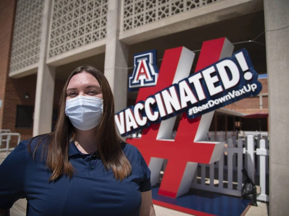 Fourth-year College of Pharmacy PharmD student Annie Hiller stands by a sign in front of the walk-in vaccination site on the University of Arizona campus. Hiller has assisted with preparing the Pfizer vaccines for distribution at the University POD.