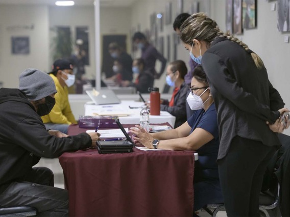 Intake staff at a COVID-19 vaccine clinic hosted by UArizona Health Sciences in the early morning hours of April 23 at the Mexican Consulate in Douglas, Ariz., as part of the Mobile Outreach Vaccination & Education for Underserved Populations, or MOVE UP, initiative. Andrea Contreras (on right in red), Maria Jaime (on right in blue), and Ana Karen Montaño (standing) register and check in Angel Loya (left in yellow) and Oscar Moreno (left in gray hat).