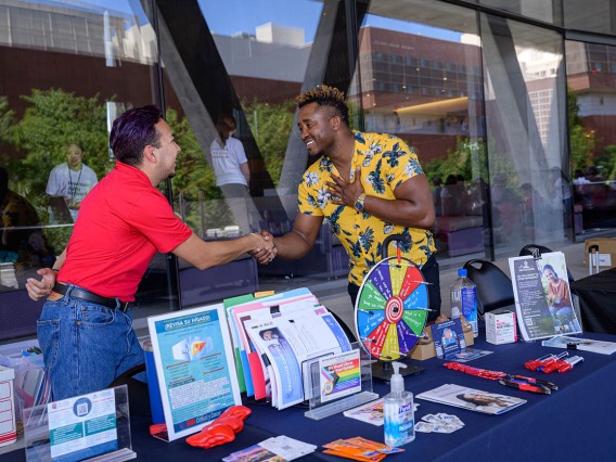 (From left) Juan Contreras II, a research program administrator, greets Tony Philippe, LL.B, a health educator, as they begin their volunteer shift at the University of Arizona Cancer Center information table at the Feast for Your Brain event.