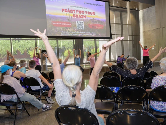 Participants at the inaugural Feast for Your Brain event take part in a group stretch between presentations in the Forum of the Health Sciences Innovation Building.