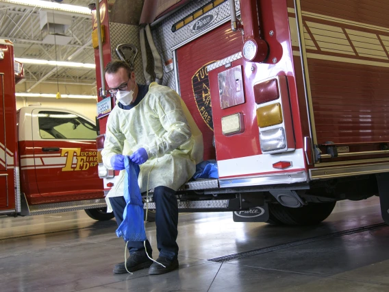 Tucson Fire Department’s Taylor Parrish puts on a protective gown and boot coverings to prevent spread of disease before entering the home a possible COVID-19 patient.