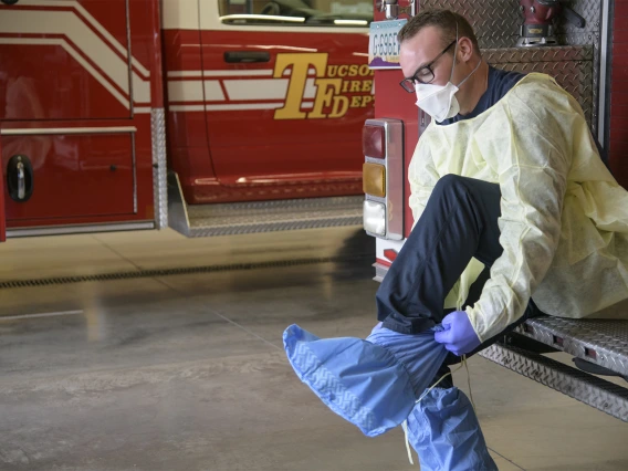 Tucson Fire Department’s Taylor Parrish puts on a protective gown and boot coverings to prevent spread of disease before entering the home a possible COVID-19 patient.