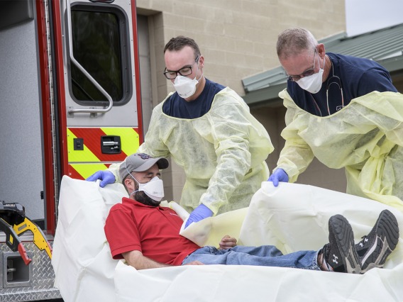 Firefighters Taylor Parrish and Chris LaFave wrap Jonathan Sexton, PhD, in a protective barrier to demonstrate how to prevent further spread of a virus during an ambulance trip to the hospital.