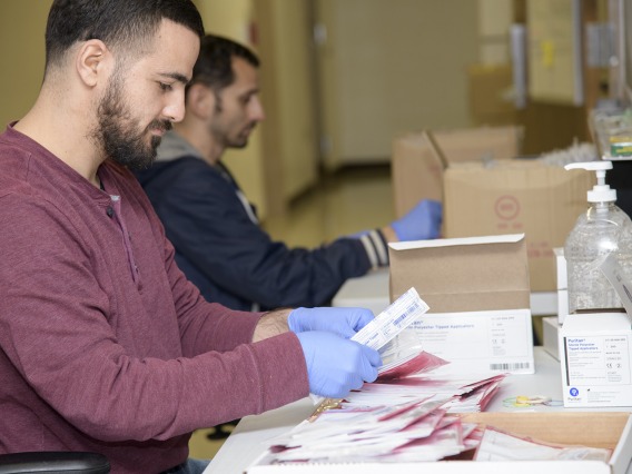 Biorepository laboratory techs Ayman Sam (left) and Brandon Jernigan (right) complete the final step to assemble the COVID-19 sample collection kit.