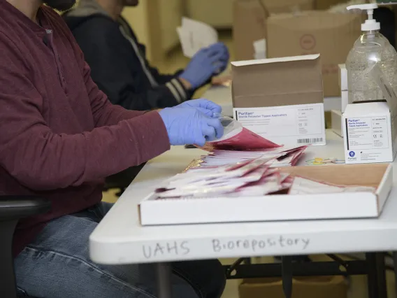 Biorepository laboratory technicians Ayman Sam (left) and Brandon Jernigan (right) complete the final step to assemble a COVID-19 sample collection kit.