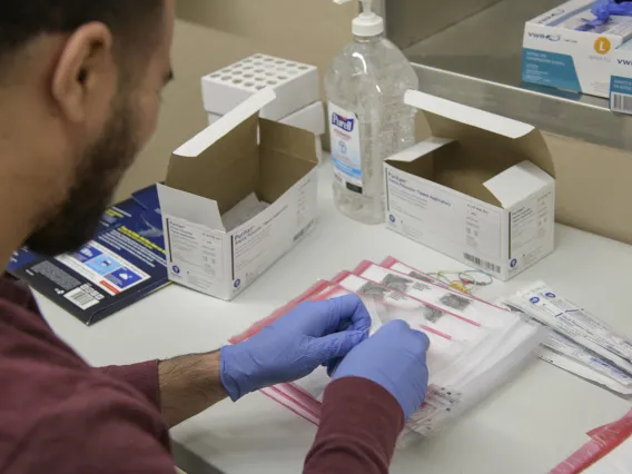 Biorepository laboratory technicians Ayman Sam (left) and Brandon Jernigan (right) complete the final step to assemble a COVID-19 sample collection kit.