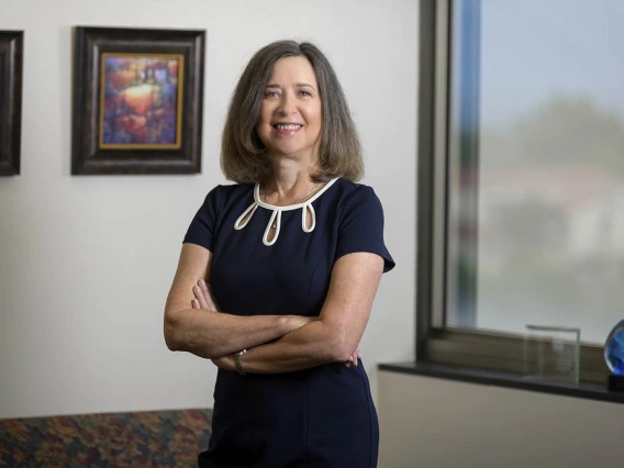 Photo of an older woman with grayish-brown hair, wearing a navy blue dress and standing in an office.