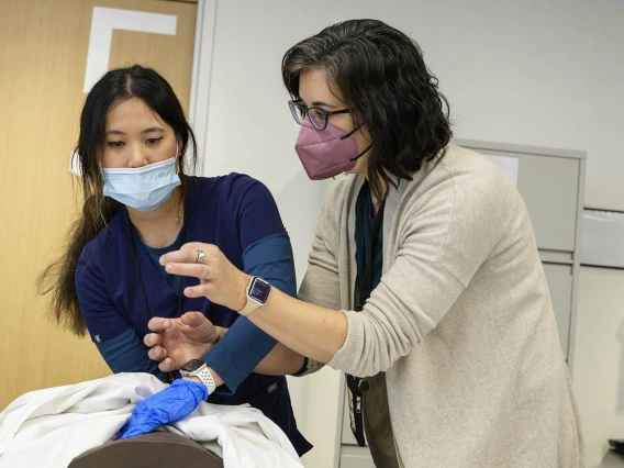 A Doctor of Nursing Practice nurse-midwifery student watches as an instructor demonstrates fundal massage on a manikin for during a clinical immersion session.