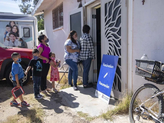 People gather outside a community center for a MOVE-UP clinic hosted by the UArizona Health Sciences in the rural town of Aguila, Ariz., to get COVID-19 vaccine shots. The mobile health unit van of the UArizona Zuckerman College of Public Health is visible in background.