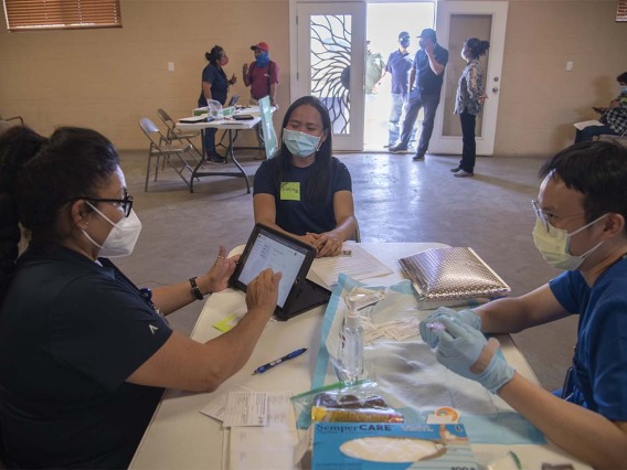 Maria Jaime, a health educator with the College of Public Health in Phoenix, goes through a patient’s answers on her registration, while vaccinator Alvin Wong, DO, an internal medicine physician with the UArizona College of Medicine – Phoenix, prepares the vaccine.