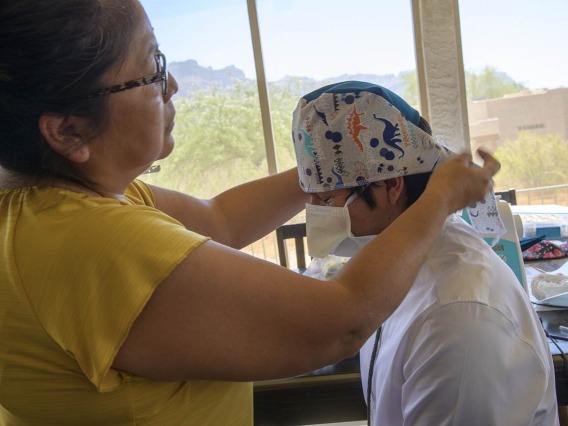 Navajo seamstress Theresa Hatathlie-Delmar checks the fit of a surgical cap on College of Medicine – Tucson student Aaron Bia.