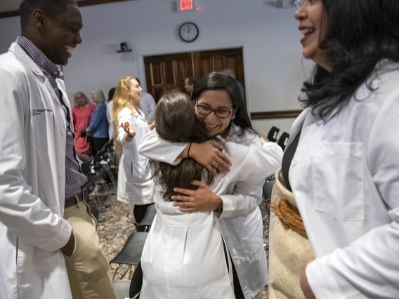 Caylan Moore, left, and Kaloni Philipp, right, watch on as Naiby Rodriguez, center, hugs China Rae Newman after the Primary Care Physician scholarship reception at El Rio in Tucson, Ariz.