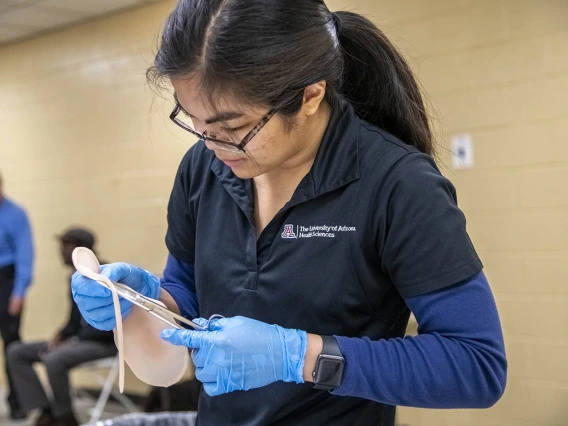 Merryl Lopido, simulation operations specialist for ASTEC, cuts synthetic skin to be placed on a volunteer to simulate a realistic-looking wound.